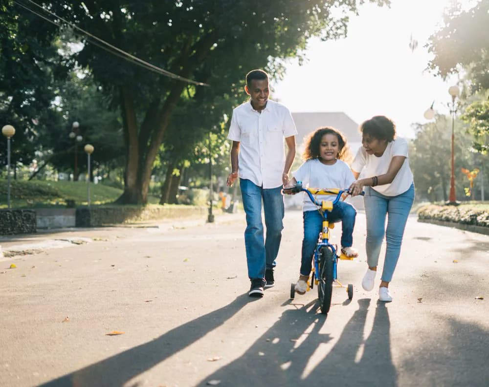 Família ensinando a filha a andar de bicicleta no fim de tarde